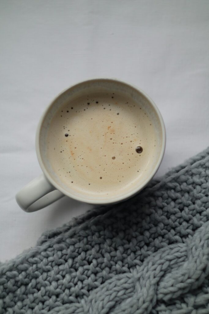 Warm drink resting on a soft textured chunky scarf in a neutral cozy setting
