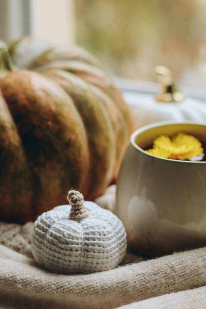 Handmade ribbed crochet pumpkin beside a warm drink on a neutral fall table